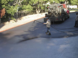 worker spraying a sealcoating on a parking lot